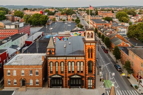 Aerial view down a tree-lined street toward a brick clock tower amid rowhomes and rooftops