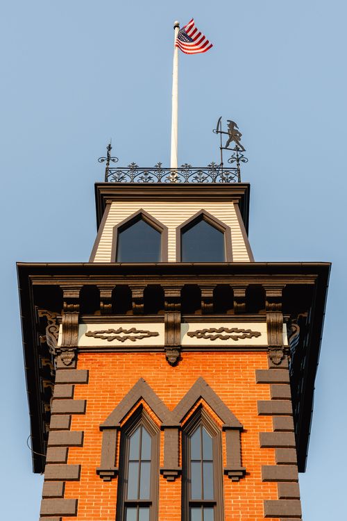 Close-up of the tower cupola with scroll brackets, an American flag and weathervane