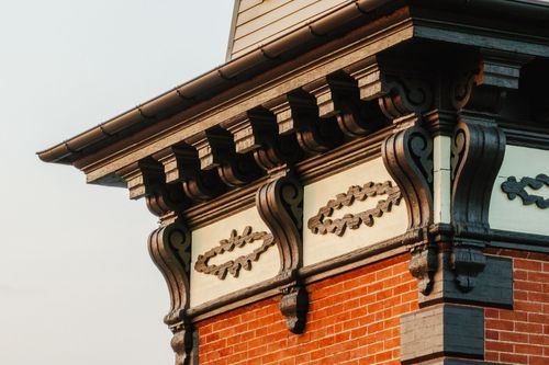 Detail of ornate roofline brackets and a carved floral medallion on red brick
