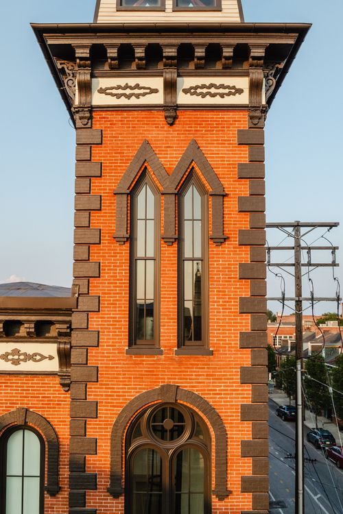 Close-up of the brick tower's twin gothic-arched windows beneath a bracketed cornice