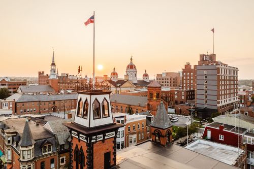 Aerial view of a rooftop flag and cupola overlooking a sunset skyline of domes and spires