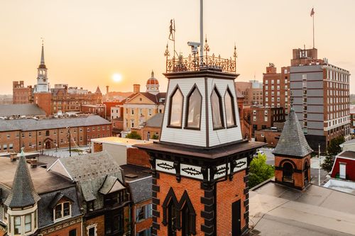 Close aerial view of an ornate weathervane-topped cupola against a warm sunset skyline