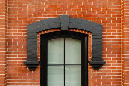 Close-up of a single arched window framed by black-painted brick voussoirs