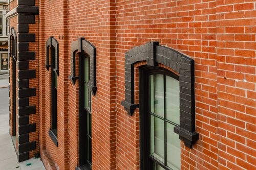 Angled view of a brick facade lined with arched windows in black-painted surrounds