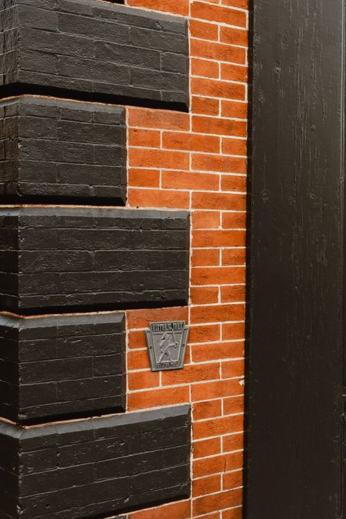 Detail of a brick corner painted in alternating black and red-brick blocks with a small plaque