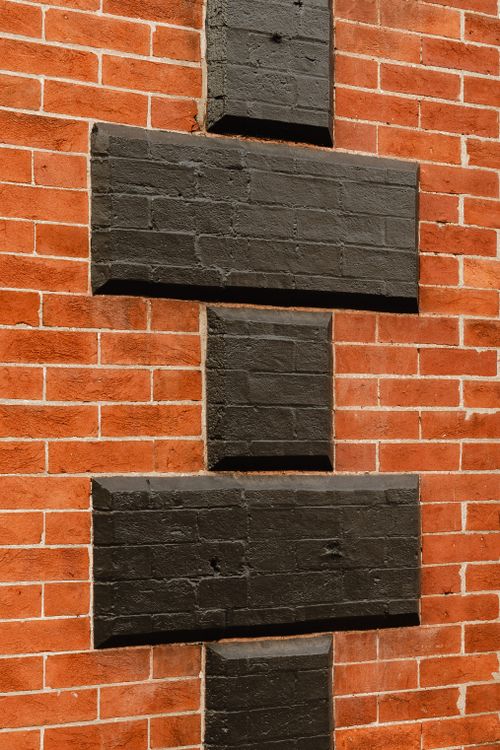 Close-up of a brick corner painted in an alternating black and terracotta block pattern