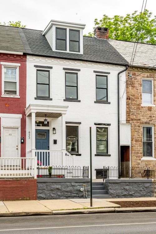White brick townhome exterior with a dormer roof, black window trim and covered entry porch