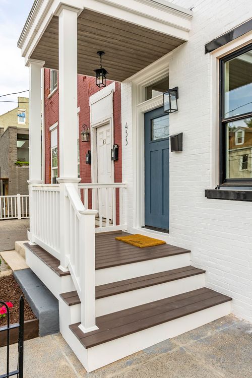Covered porch steps with wood decking beside a red brick neighboring rowhome
