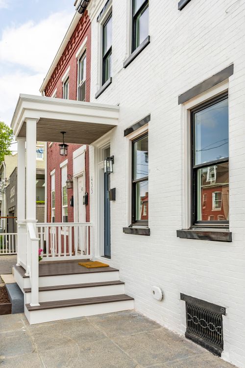 Angled view of a white brick rowhome facade with black-trimmed windows beside a red brick neighbor