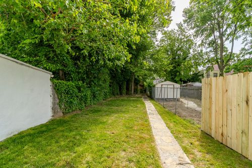 Long grassy backyard bordered by trees and a stone walkway leading to a rear shed