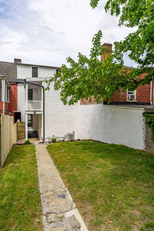 Rear facade of a white stucco addition with a balcony overlooking a landscaped backyard