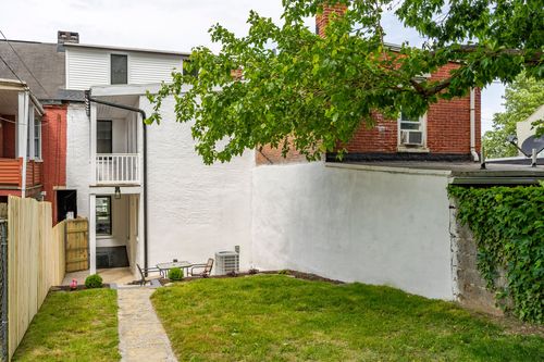 White stucco rear addition with balcony, patio seating and a neighboring brick building