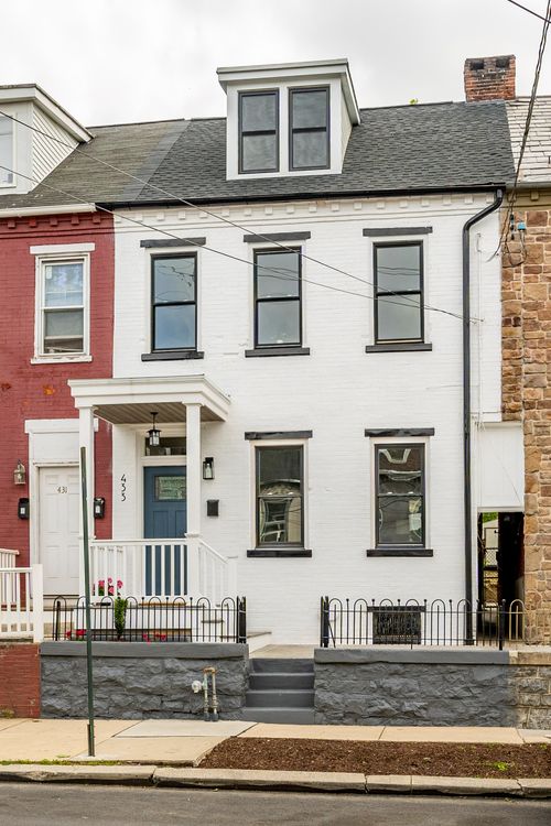 White brick rowhome facade beside a red brick neighbor, with black-trimmed windows and covered porch