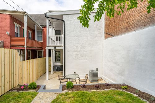 Rear white stucco addition with a second-floor balcony above a patio table and fenced yard