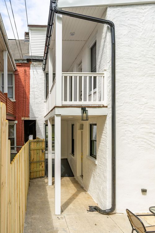 Two-story rear addition with a covered balcony above a ground-level entry and wood fence