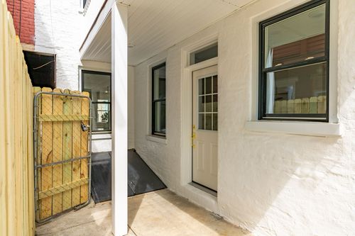 Covered rear walkway with a paneled white door and black-trimmed windows along a stucco wall