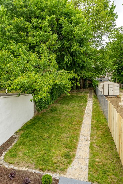 Shaded backyard with mature trees and a stone path leading to a storage shed