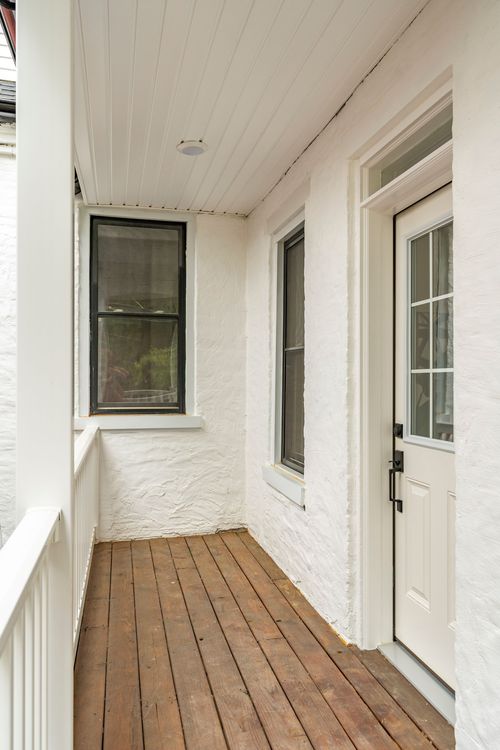 Covered wood-plank balcony with black-trimmed window beside a paneled white entry door