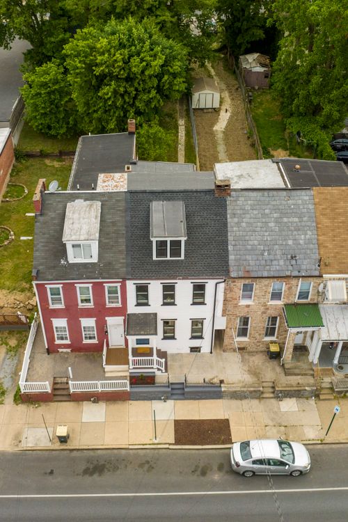 Aerial view of a red brick rowhome roof with dormer windows above a shaded rear yard