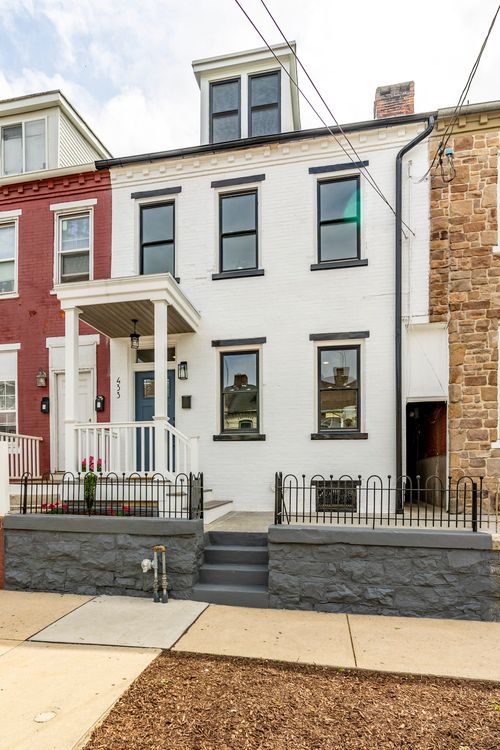White painted brick townhome with black window trim, covered porch and wrought iron fence