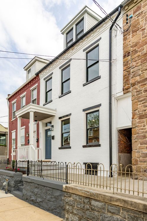 Side angle of a white brick rowhome beside a red brick and a stone-faced neighbor