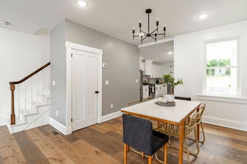 Open dining area beside a wood staircase with white paneled door and hardwood floors