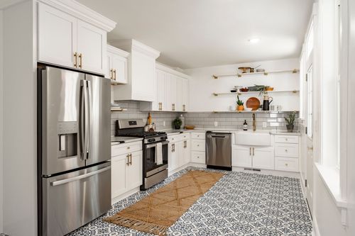 White kitchen with stainless steel appliances, gold hardware and patterned tile floor