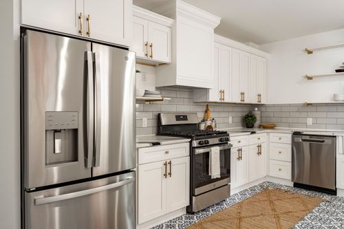 Kitchen with white shaker cabinets, brass hardware and gray subway tile backsplash