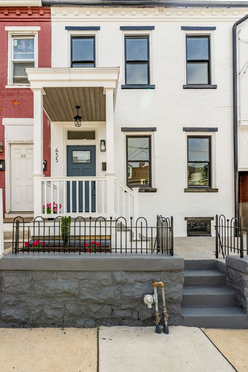 White brick townhome facade with slate-blue front door and black shutters under a gray sky