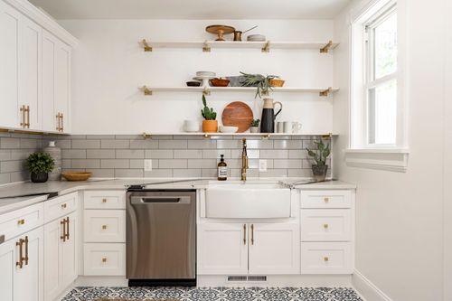 Close-up of open wood shelving with decor above a white farmhouse sink and brass faucet