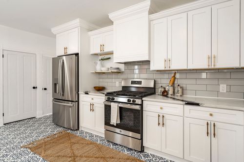 Kitchen range wall with white cabinetry, gas stove and patterned tile floor
