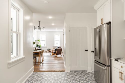 View through a kitchen hallway toward a dining room with a round table and black chandelier