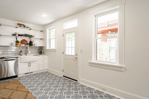 White kitchen corner with open shelving, a farmhouse sink and patterned tile floor near the back door