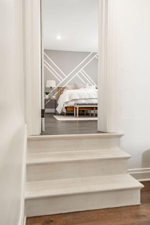View up a white staircase toward a bedroom with a geometric gray and white accent wall