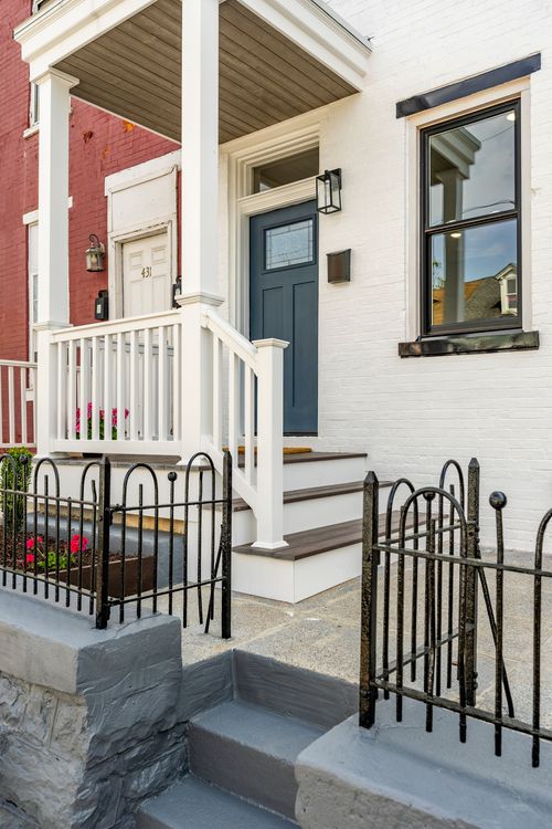 Close-up of a covered front porch with white railings, wood steps and a slate-blue door