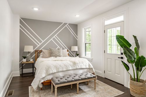 Bedroom with a geometric gray and white accent wall, wood bed frame and tufted bench