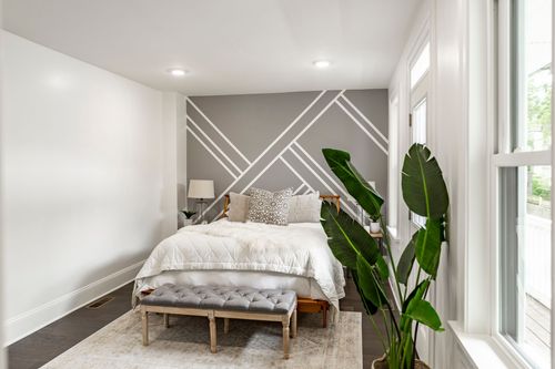 Bedroom with a geometric accent wall, upholstered bed and a large potted plant by the window