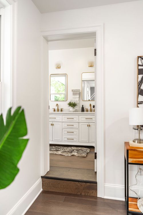 View through a bedroom doorway into a bathroom with a dual vanity and gold-framed mirrors