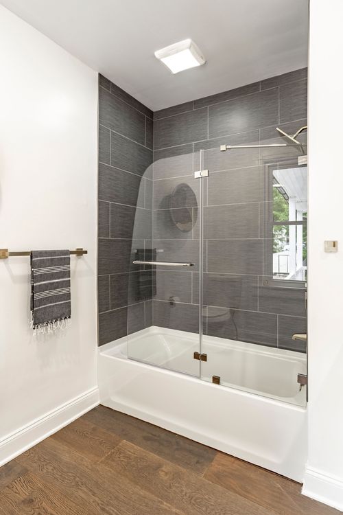 Glass-enclosed tub and shower with gray tile surround and a striped hand towel