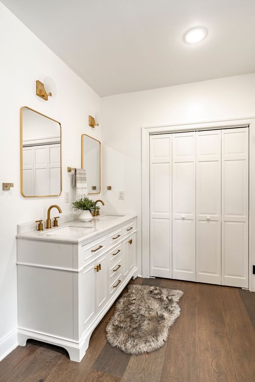 Primary bathroom with a white double vanity, oval gold mirrors and a faux fur rug