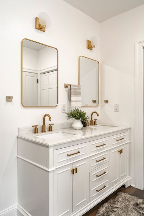 Close-up of a white double vanity with brass fixtures, gold mirrors and marble countertop