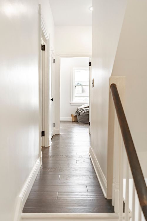 Hallway with dark wood flooring leading to a bedroom doorway and window