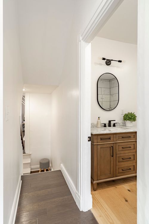 Hallway view down a staircase toward a powder room with a wood vanity and oval mirror
