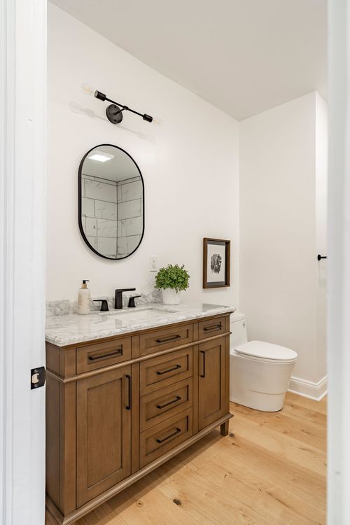Powder room with a stained wood vanity, black fixtures, oval mirror and marble counter