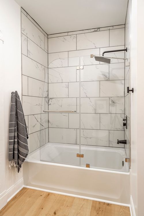 Tub and shower with white marble-look tile surround, glass panel and matte black fixtures