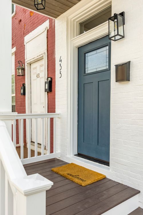 Close-up of a slate-blue front door with glass panel, house numbers and sconce lighting