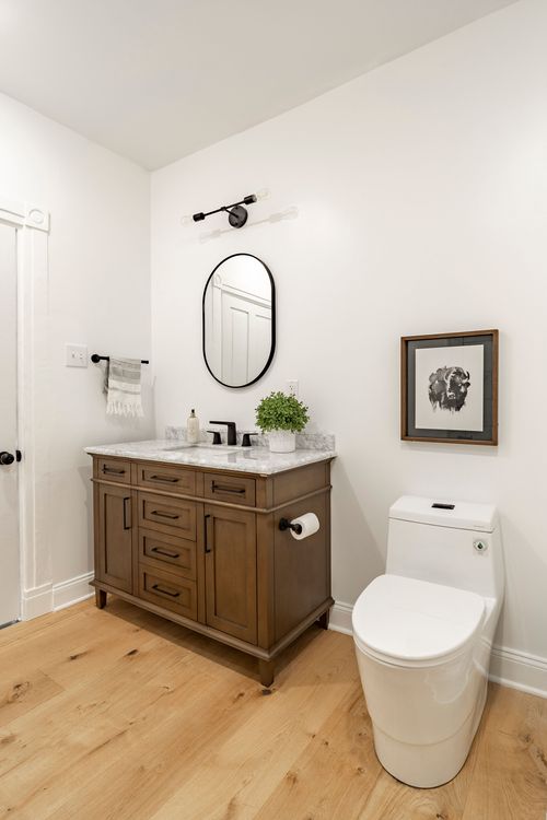 Powder room with a stained wood vanity, oval black mirror and framed animal print