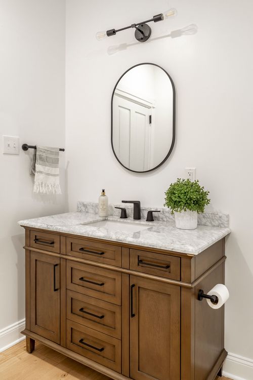 Close-up of a stained wood vanity with a black oval mirror and marble countertop
