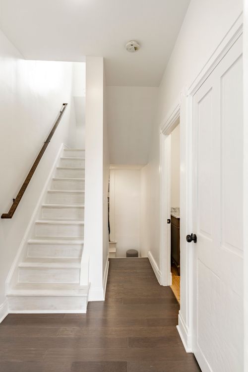 Staircase with white painted treads and a wood handrail leading down to a hallway