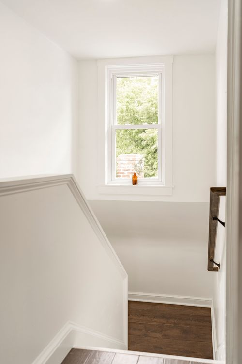 Narrow attic stairwell lit by a small window with a dark wood handrail